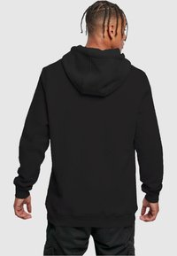 Black hoodie with a drawstring hood, ribbed cuffs, and hem. Soft fabric texture and relaxed fit. Back view showing simple design details.