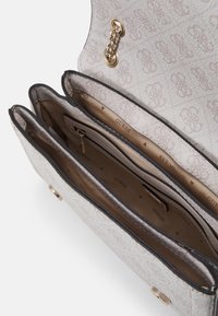 Light gray handbag with fabric texture, featuring three compartments, gold hardware, and a patterned interior lining with the "GUESS" logo.