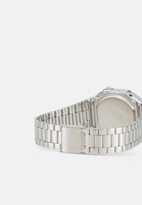 Montre en acier inoxydable argenté avec un bracelet à maillons, un boîtier rectangulaire et une boucle simple. L'arrière de la montre est visible, présentant un design minimaliste.