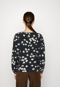 Bluse med blomstermønster og lange ærmer, i marineblå stof med hvide blomster og grønne blade, med rund halsudskæring og afslappet pasform.