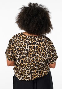 Top en imprimé léopard avec des manches courtes, un décolleté large et une coupe ample. Les couleurs dominantes sont le noir, l'or et le beige.