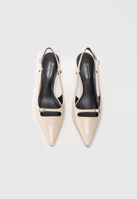 Beige vegan leather slingback shoes with pointed toes, cut-out details, and a small metal buckle accent on the ankle strap.