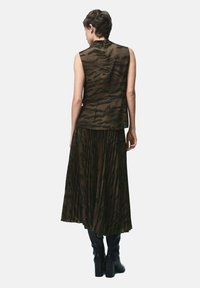 Top sin mangas con un estampado animal oscuro, combinado con una falda plisada en tonos a juego, complementado por botas negras hasta la rodilla.