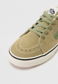 Baskets en suede vert avec une forme arrondie, des perforations décoratives, des coutures contrastantes et une semelle en caoutchouc blanc avec un accent noir.