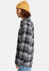 Gray and black plaid flannel shirt with yellow accents, long sleeves, and a button-down collar. Worn with a tan beanie.
