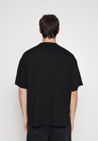 Svart bomull T-shirt, oversized passform, korta ärmar, rund halsringning, enkel design, synlig sömnad vid fållen, bakvy.