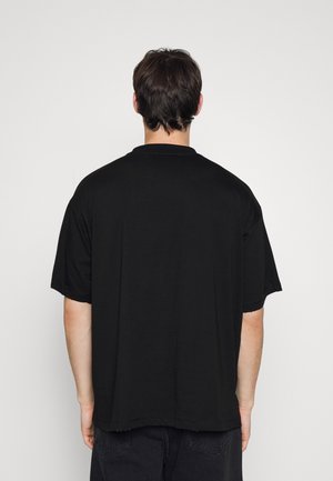 Černé bavlněné tričko, volný střih, krátké rukávy, kulatý výstřih, jednoduchý design, viditelné švy na lemu, zadní pohled.