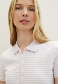 Svetlofialová pruhovaná polo košela s jemnou textúrou, ktorá má golier a šest ružových gombíkov na prednej strane.