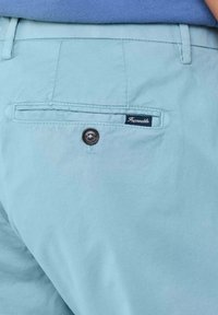 Pantalones cortos de color azul claro con una textura suave, que presentan un bolsillo trasero con un botón y una etiqueta de la marca cosida en el borde del bolsillo.