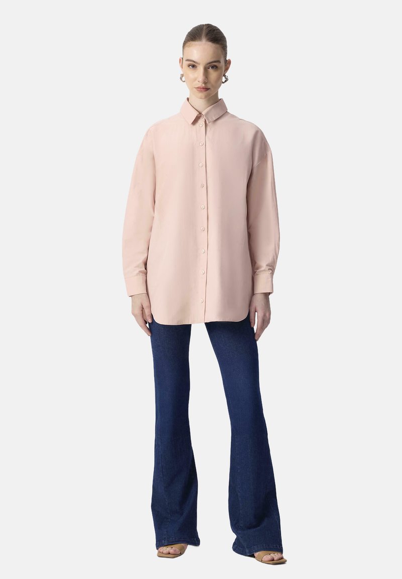 Ljusrosa långärmad skjorta med krage, kombinerad med mörkblå utsvängda jeans. Outfiten har en mjuk textur och en avslappnad passform.