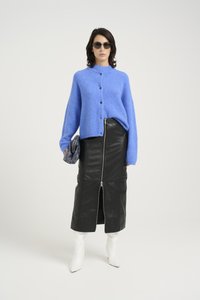 Blue knitted cardigan with buttons, black leather skirt with front zipper, white pointed boots, gray textured clutch, and sunglasses.