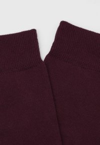 Burgunderfarbene Stricksocken mit geripptem Bund, die eine glatte Textur und ein nahtloses Design aufweisen, in V-Form auf einem hellen Hintergrund gefaltet.