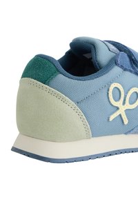 Zapatilla que presenta una combinación de malla azul suave y ante verde, con un talón verde claro y un logo amarillo. Forma redondeada con acentos texturizados.