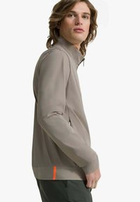 Giacca beige con colletto alto, vestibilità slim, tasche laterali e un accento arancione all'orlo. Tessuto liscio, materiale leggero.