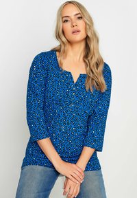 Sininen leopardikuosiset paita, jossa on kolmenneljänneksen hihat, pyöreä pääntie ja nappi- yksityiskohta. Pehmeää kangasta, rento istuvuus ja hienovarainen tekstuurimalli.