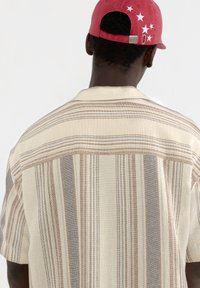 Chemise à manches courtes crème avec des rayures verticales marron et gris, dotée d'un tissu texturé et d'un design de col classique.