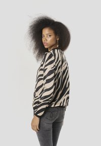 Dierenprint blouse in beige en zwart, met lange mouwen en een losse pasvorm. Gecombineerd met donkergrijze strakke jeans.