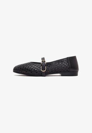 Zapato plano negro con un patrón perforado de diamantes, una correa con hebilla lateral y un tacón bajo, visto desde el lado exterior.