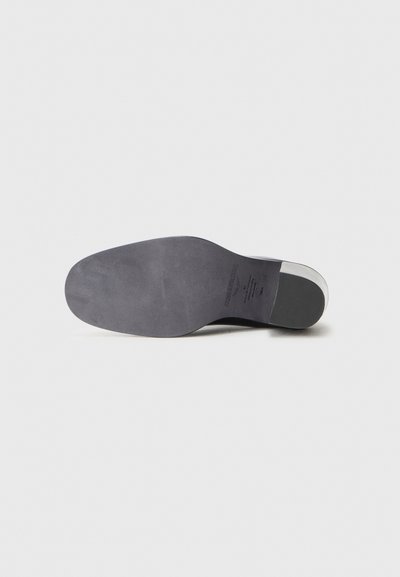 Sula av sko med en slät matt yta, rundad form, mörk färg och en lätt upphöjd del vid hälen. Texturerade ytdetaljer synliga.