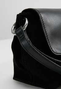 Sac à main en cuir et daim noirs avec un anneau métallique argenté reliant la poignée au corps du sac.