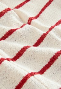 Tissu tricoté blanc avec des motifs rayés rouges courant en diagonale. La texture semble douce et légèrement duveteuse.