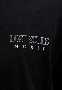 Czarny T-shirt z napisem "LOST SOULS" i "MCXII" w białym kolorze. Materiał wydaje się gładki, z klasycznym dekoltem w kształcie łódki.