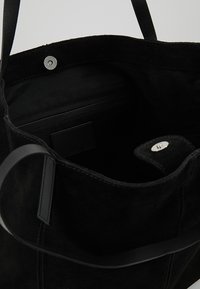 Czarna torba tote z zamszu z skórzanymi akcentami, wewnętrzną kieszenią i zapięciem na zatrzask. Gładka tekstura z solidnymi uchwytami, o minimalistycznym designie.