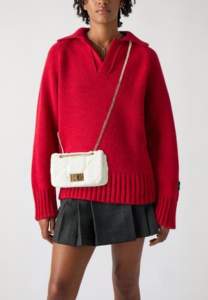 Pulover roșu tricotat cu decolteu în V și tivul cu chenar, asortat cu o geantă albă tip crossbody, matlasată, cu o închidere din aur și curea din lanț.