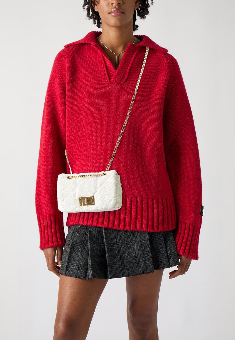 Červený pletený sveter s výstrihom do V a rebrovaným lemom, doplnený bielou prešívanou crossbody taškou s zlatým zámkom a reťazovým popruhom.