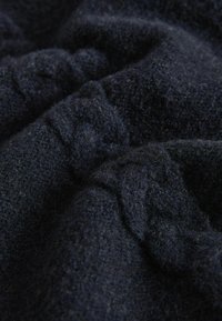 Jūras zils vilnas audums ar mīkstu, strukturētu virsmu, redzamiem šķiedru pavedieniem un viegli saburzītu izskatu.