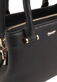 Zwarte leren handtas met een gestructureerd oppervlak, gouden hardware, bovenhandvatten en een ritsluiting. Bevat een klein decoratief logo.