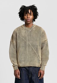Light brown knitted sweater with a ribbed texture, dropped shoulders, and a crew neckline. Accented by a subtle vertical stripe pattern.