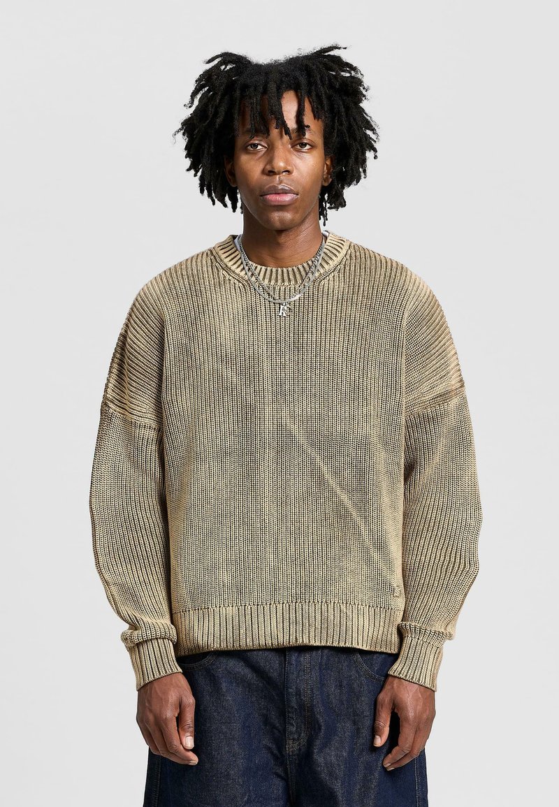 Light brown knitted sweater with a ribbed texture, dropped shoulders, and a crew neckline. Accented by a subtle vertical stripe pattern.