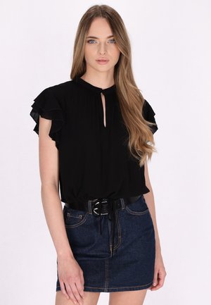 Blusa nera con maniche a rouches e scollatura a chiave, abbinata a una mini gonna di denim con una cintura nera e cuciture visibili.