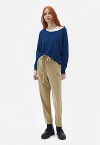 Blauwe lange mouwen top met een ronde hals en een losse pasvorm, gecombineerd met tan tapered broek en zwarte veterschoenen.