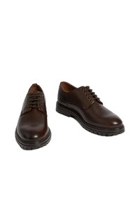 Zapatos de cuero marrón con un acabado liso, punta redonda y seis ojetes para los cordones. Presenta una suela de goma gruesa con un patrón de rodadura.