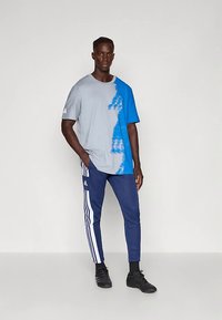 Camisola atlética cinza e azul com design em degradê, combinada com calças de treino azuis-marinho com riscas laterais brancas e um pequeno logótipo.