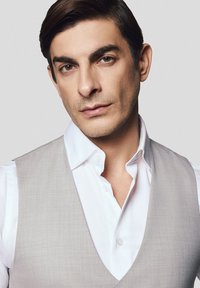 Szary kamizelka na białej koszuli z klasycznym kołnierzykiem i dopasowanym krojem, gładka tekstura, z wyraźnymi detalami przeszyć na brzegach.