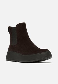 Botines de ante negro con una suela negra gruesa, que presentan paneles laterales elásticos para ponérselos fácilmente y un acabado liso y texturizado.