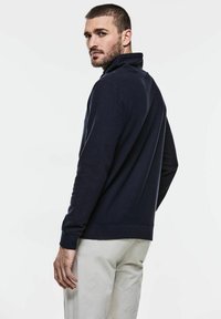 Námořnický modrý pulovrový svetr s vysokým límcem, dlouhými rukávy a žebrovanými manžetami a spodním lemem. Měkký materiál, volný střih.