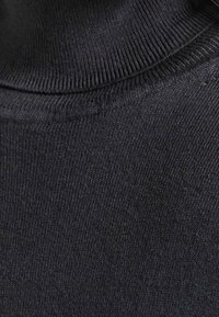 Pull à col roulé gris foncé avec un col côtelé et une texture lisse, présentant un gros plan du motif finement tricoté du tissu.