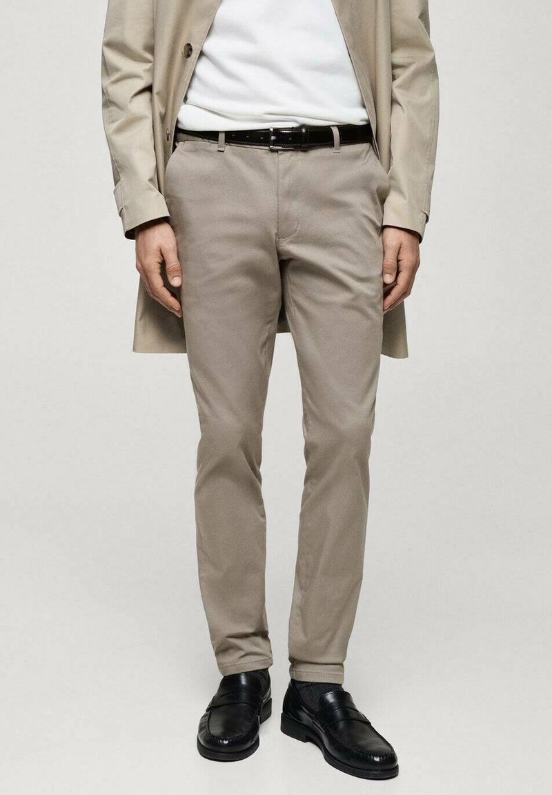 Světlé béžové kalhoty z měkké látky, s přizpůsobeným střihem a hladkou texturou. Nošeny s bílým svetrem a černými koženými botami.