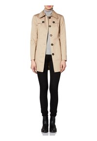 Béžový trenčkot s límcem a knoflíkovým zapínáním, s dlouhými rukávy a rovný střih. Nosený přes šedý rolák a černé kalhoty.