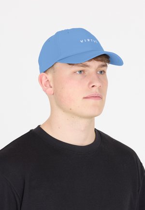 Junger Mann mit heller Haut und blauen Augen, der eine blaue Baseballkappe mit dem Schriftzug „VIRTUS“ und ein schlichtes schwarzes Rundhalsshirt trägt.
