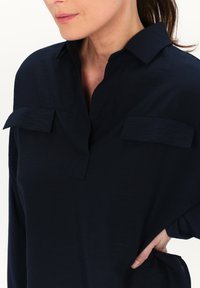 Navyblaues Hemd aus leichtem Stoff, mit einem Kragen, zwei Brusttaschen und einem lockeren Schnitt mit hochgekrempelten Ärmeln.