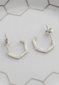 Silver hexagonformade örhängen med en polerad yta och en enkel design, som har en säker post och baksida.