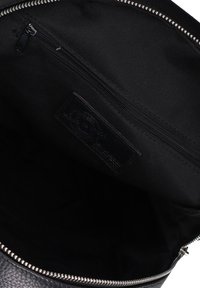 Interno di una borsa in pelle nera che mostra una tasca interna con zip e foderato in tessuto con i denti della zip argentati visibili lungo il bordo superiore.