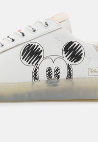 White sneaker featuring a large black Mickey Mouse graphic, smooth material, and a translucent sole with subtle texture and design accents.