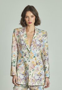 Blazer stampato floreale realizzato in un tessuto leggero e texture con colori vivaci. Elementi distintivi includono un profondo scollo a V e due tasche frontali.