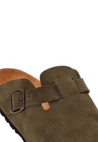 Zueco de ante verde oliva con correa ajustable de hebilla, plantilla de cuero marrón y suela de goma negra texturizada. Diseño clásico de slip-on.